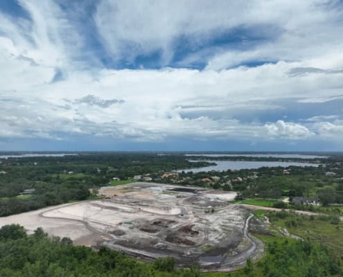 Aerial view of a construction site for site development and infrastructure projects with green surroundings and water bodies in the background.
