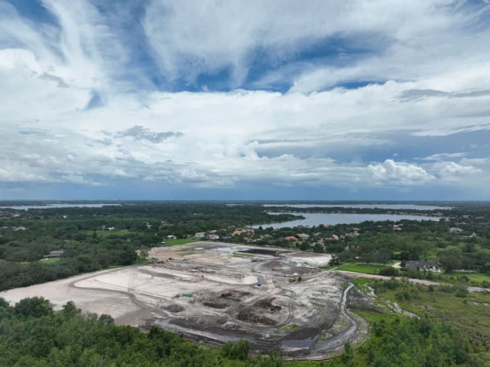 Aerial view of a construction site for site development and infrastructure projects with green surroundings and water bodies in the background.