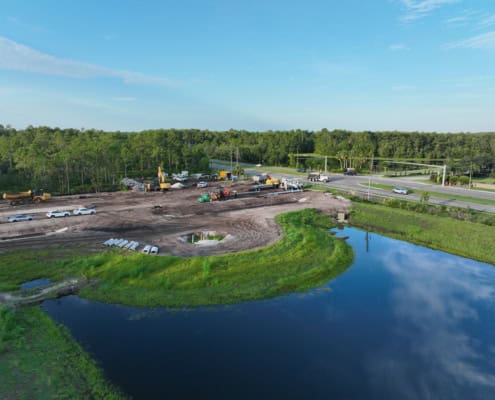 Modern site development with ongoing construction on cleared land near water body, combining urban planning and landscape design, showcasing infrastructure improvement and environmental integration.