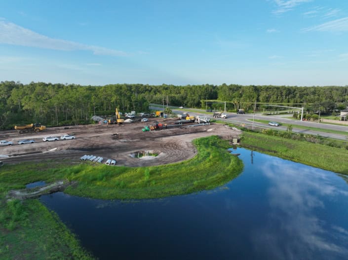 Modern site development with ongoing construction on cleared land near water body, combining urban planning and landscape design, showcasing infrastructure improvement and environmental integration.