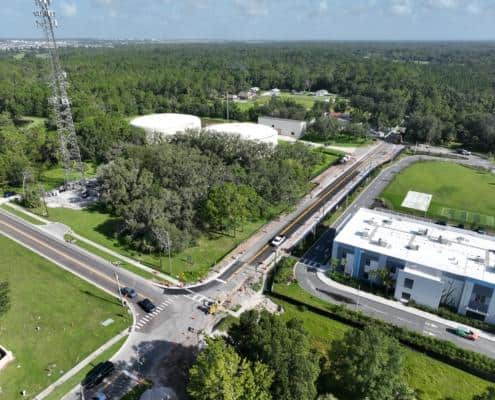 Aerial view of site development for infrastructure projects, showcasing road construction, utility upgrades, and landscaping in a suburban area with greenery and residential buildings.
