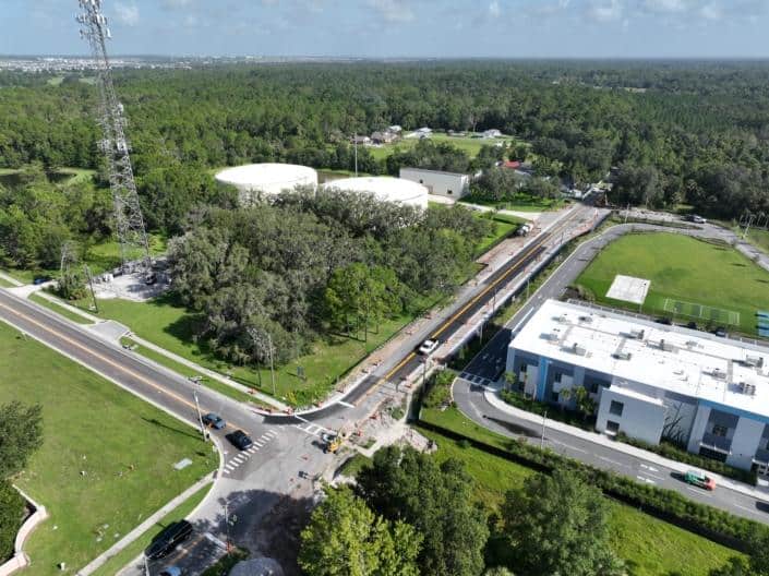 Aerial view of site development for infrastructure projects, showcasing road construction, utility upgrades, and landscaping in a suburban area with greenery and residential buildings.