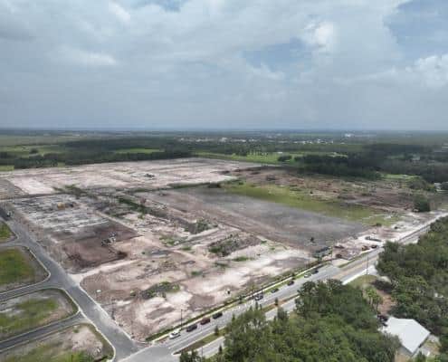 Aerial view of a cleared construction site for new development in a lush green area, prepared for building with heavy machinery and infrastructure setup, under partly cloudy skies.