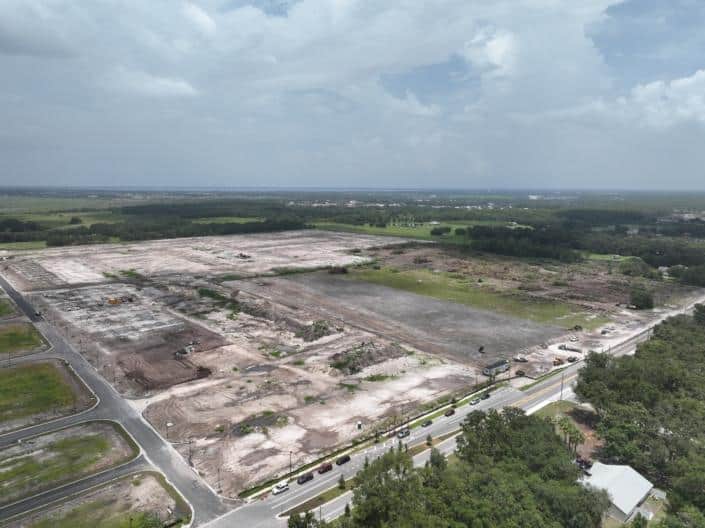 Aerial view of a cleared construction site for new development in a lush green area, prepared for building with heavy machinery and infrastructure setup, under partly cloudy skies.