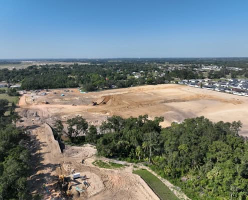 Aerial view of commercial site development with earth-moving equipment, cleared land for construction, and surrounding greenery, showcasing professional site development services for new projects.