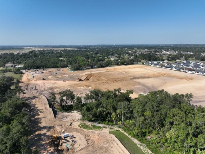 Aerial view of commercial site development with earth-moving equipment, cleared land for construction, and surrounding greenery, showcasing professional site development services for new projects.