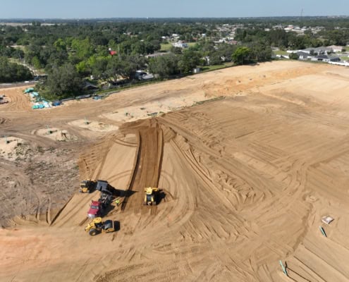 Site development construction with heavy machinery on cleared land for new residential or commercial project, showing earthmoving and grading for infrastructure preparation.