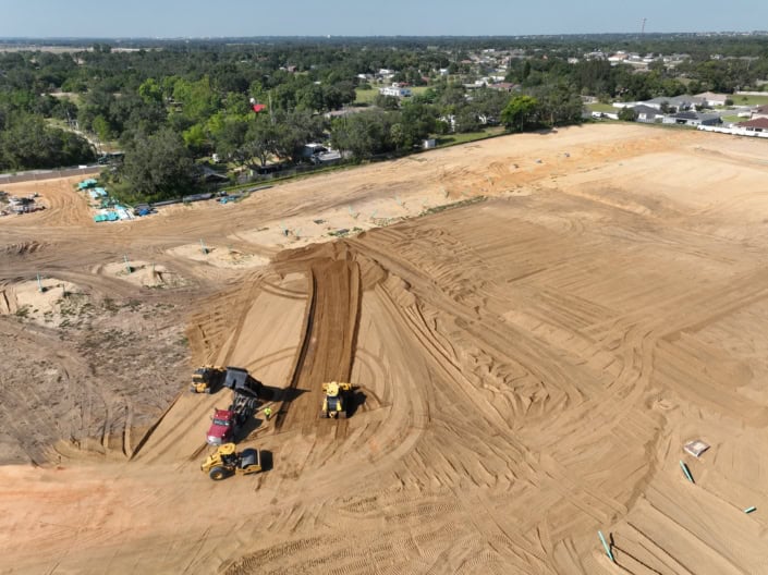 Site development construction with heavy machinery on cleared land for new residential or commercial project, showing earthmoving and grading for infrastructure preparation.
