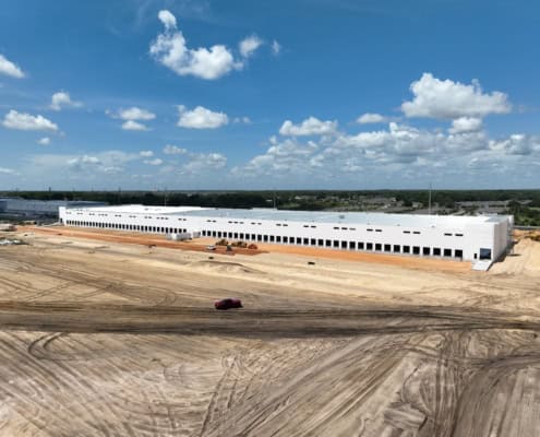 Modern industrial warehouse under construction on spacious lot with heavy machinery and dirt roads, showcasing site development and commercial building construction.