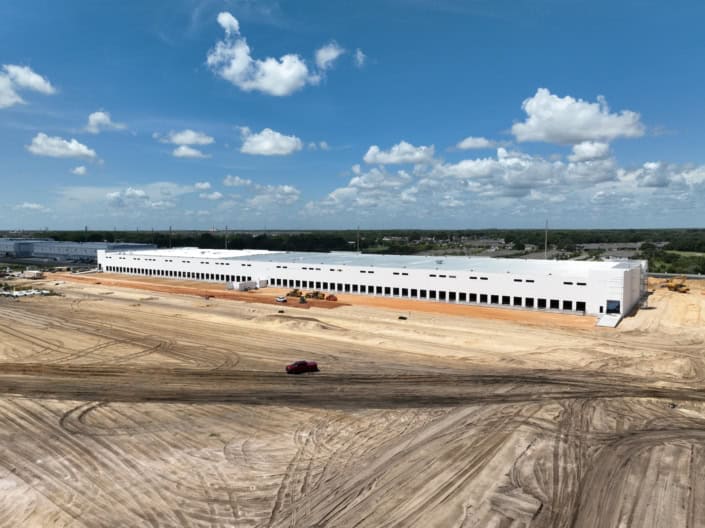 Modern industrial warehouse under construction on spacious lot with heavy machinery and dirt roads, showcasing site development and commercial building construction.