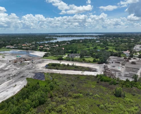 Aerial view of a residential land development site under construction with heavy equipment and excavation activities near water bodies and greenery.