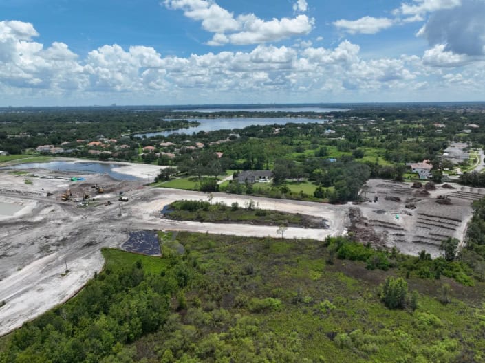 Aerial view of a residential land development site under construction with heavy equipment and excavation activities near water bodies and greenery.