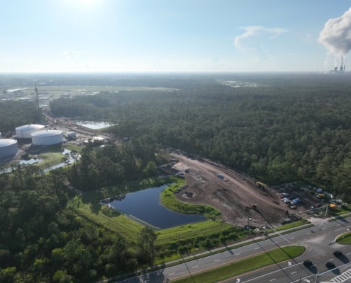 Industrial site development with construction equipment, a pond, and surrounding greenery, showcasing expert site development services for commercial and industrial projects.