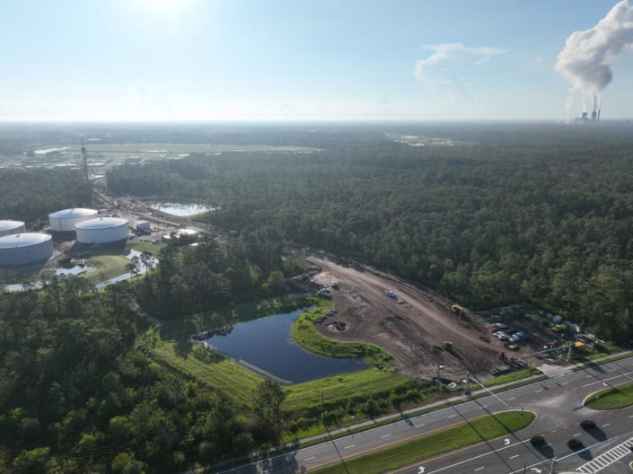 Industrial site development with construction equipment, a pond, and surrounding greenery, showcasing expert site development services for commercial and industrial projects.