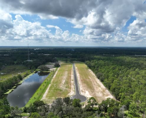 Serene site development with water feature, paved roads, and lush green forestry, showcasing professional land clearing and infrastructure services for commercial or residential projects in Florida.