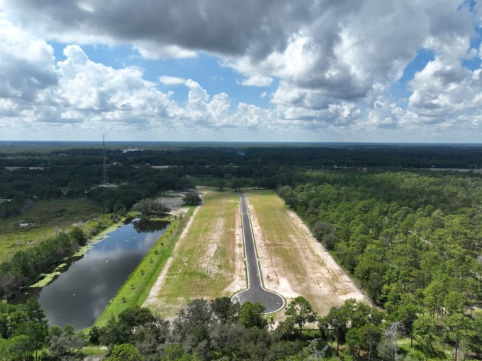 Serene site development with water feature, paved roads, and lush green forestry, showcasing professional land clearing and infrastructure services for commercial or residential projects in Florida.