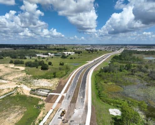 Wide aerial view of a new highway construction project with ongoing development and greenery in the area under sunny skies.