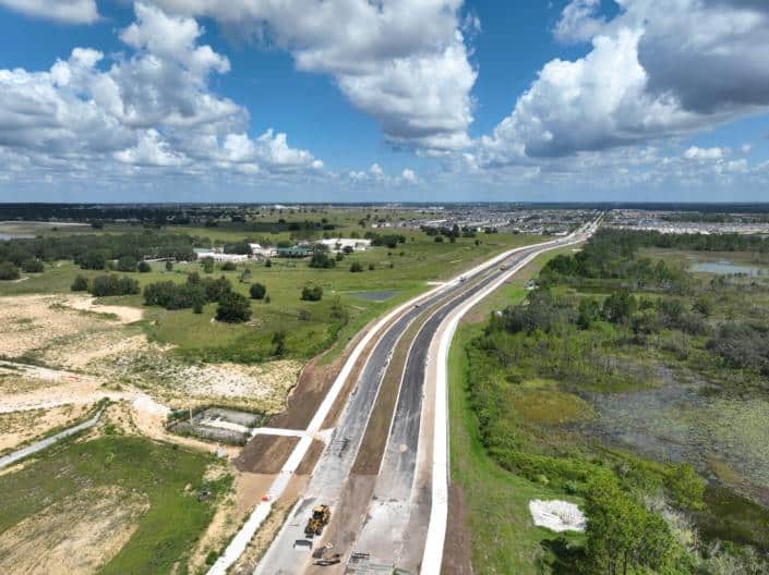 Wide aerial view of a new highway construction project with ongoing development and greenery in the area under sunny skies.