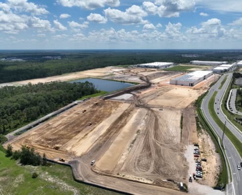 Large industrial site development with cleared land, construction equipment, and commercial warehouses under construction, showcasing site development services.