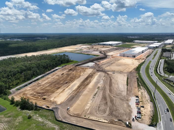 Large industrial site development with cleared land, construction equipment, and commercial warehouses under construction, showcasing site development services.