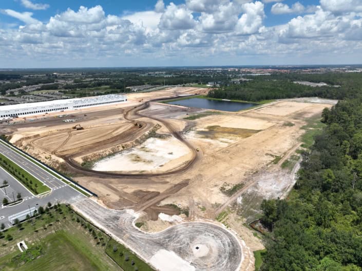 Excavation site for commercial development with heavy machinery, cleared land, and a pond in a suburban area.