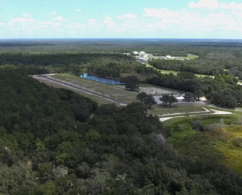 Aerial view of a site development project with cleared land, water features, and surrounding forests, showcasing infrastructure and construction progress for sustainable land use.