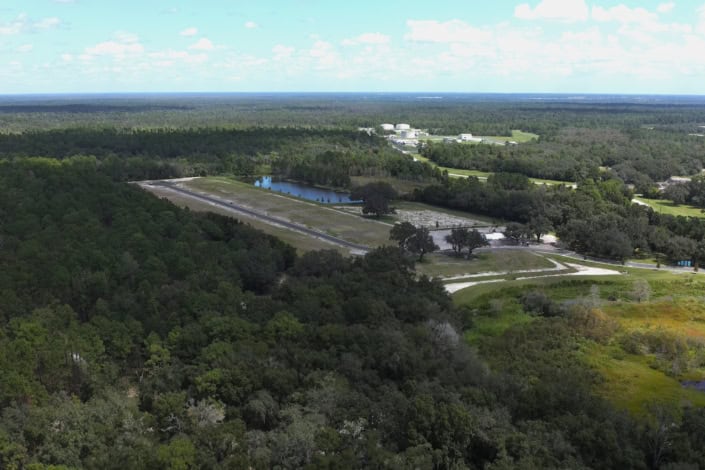 Aerial view of a site development project with cleared land, water features, and surrounding forests, showcasing infrastructure and construction progress for sustainable land use.
