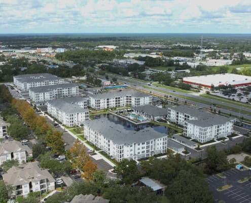 Modern apartment complex with a central pool and landscaped areas, located in a busy urban setting with shopping centers and major roads nearby.