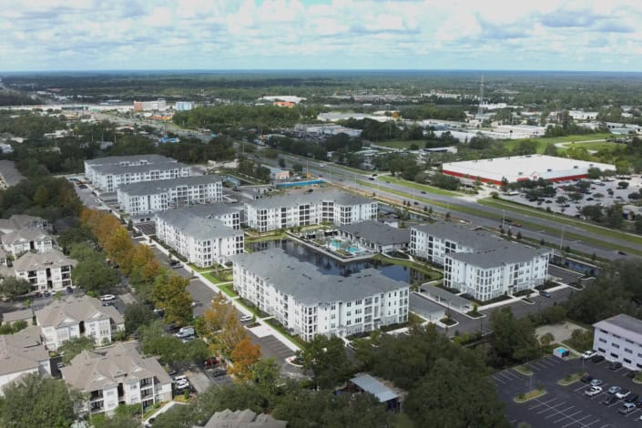 Modern apartment complex with a central pool and landscaped areas, located in a busy urban setting with shopping centers and major roads nearby.