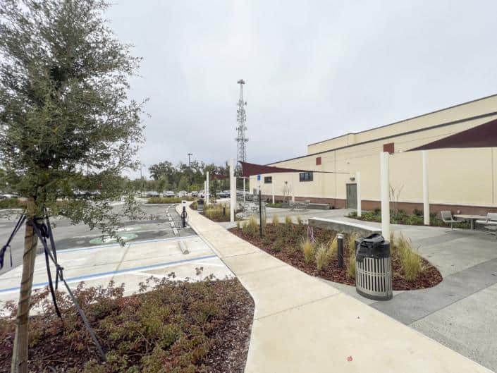 Modern commercial building exterior with landscaped surroundings, outdoor seating, and electric vehicle charging station.