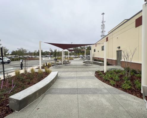 Modern outdoor seating area with shade sails, concrete walkways, and surrounding greenery, designed for community gatherings and customer comfort at SDC Site Development.