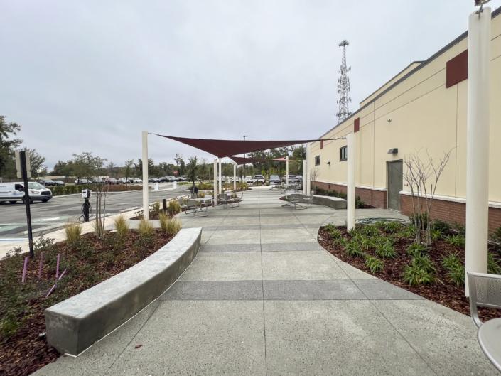 Modern outdoor seating area with shade sails, concrete walkways, and surrounding greenery, designed for community gatherings and customer comfort at SDC Site Development.
