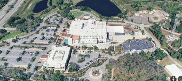 Modern site development and construction project at a large educational facility with parking, landscaping, and surrounding greenery.