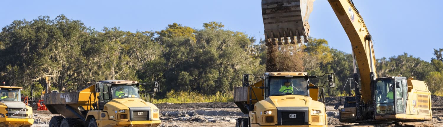 Excavator and construction trucks working on land development for commercial or industrial site preparation.