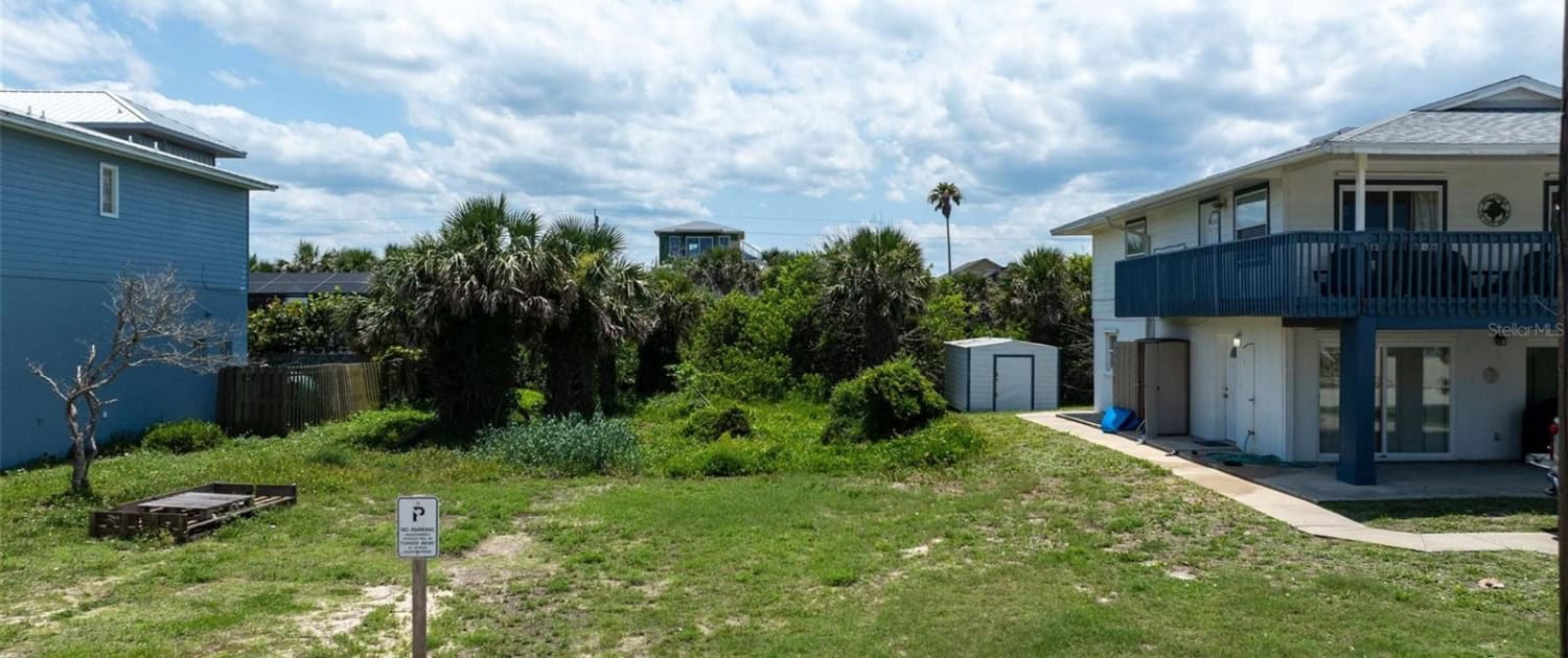 A backyard with a grassy area, palm trees, and neighboring houses, showcasing site development and outdoor space planning for residential properties.