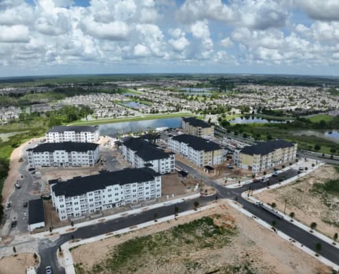 Aerial view of a residential site development with multi-story apartment buildings under construction, surrounded by water bodies, greenery, and new paved roads, showcasing modern site development techniques.
