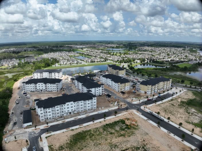 Aerial view of a residential site development with multi-story apartment buildings under construction, surrounded by water bodies, greenery, and new paved roads, showcasing modern site development techniques.