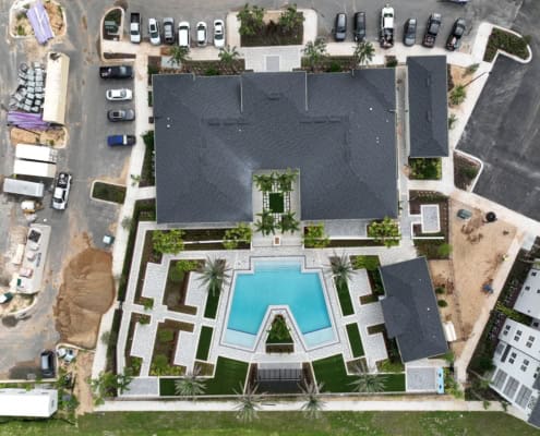 Modern commercial building with landscaped outdoor areas, swimming pool, and parking lot during construction, showcasing site development and architectural planning.