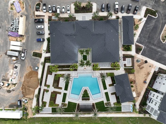 Modern commercial building with landscaped outdoor areas, swimming pool, and parking lot during construction, showcasing site development and architectural planning.