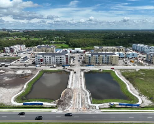 Modern mixed-use construction site with apartment buildings, parking, and water features, showcasing comprehensive site development services for residential communities.