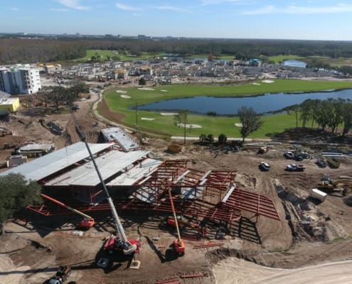 Modern construction site with steel framework, cranes, and ongoing development of a luxury residential community near a golf course and water features.