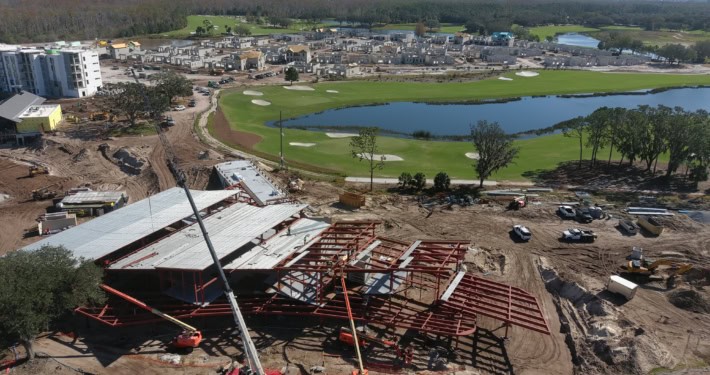 Modern construction site with steel framework, cranes, and ongoing development of a luxury residential community near a golf course and water features.