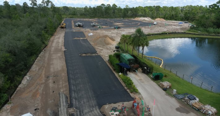 Newly paved roadway construction by SDC Site Development, focusing on commercial infrastructure and landscaping near a pond.