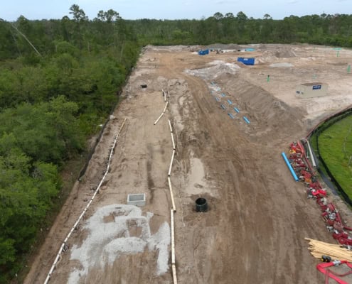 Excavation site for commercial development with piping and foundation preparation, surrounded by lush green trees, illustrating early stages of site development services.