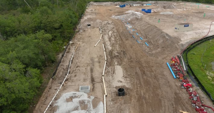 Excavation site for commercial development with piping and foundation preparation, surrounded by lush green trees, illustrating early stages of site development services.
