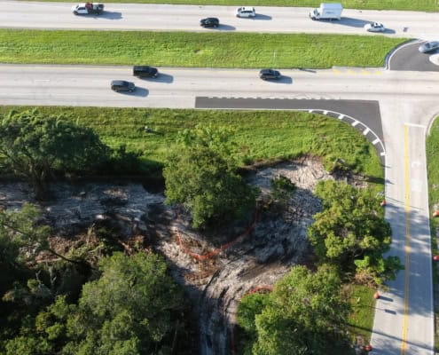 Excavation site for new road development with surrounding greenery and traffic lanes, showcasing site preparation services for infrastructure projects.