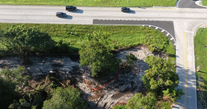 Excavation site for new road development with surrounding greenery and traffic lanes, showcasing site preparation services for infrastructure projects.
