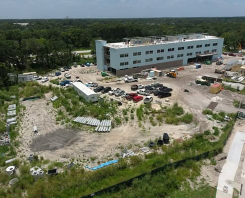 Modern commercial building under construction with surrounding parking lot and construction materials, showcasing site development and infrastructure work.