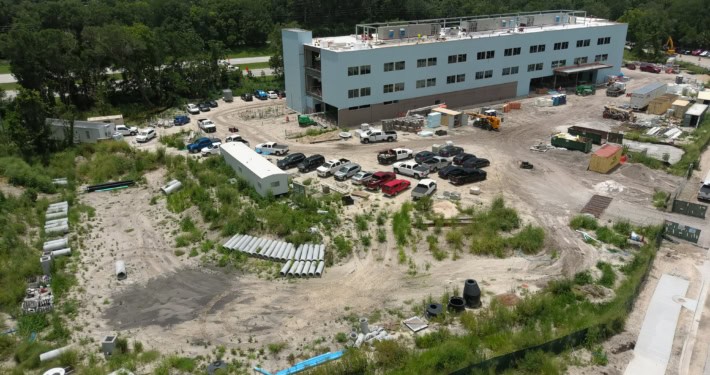 Modern commercial building under construction with surrounding parking lot and construction materials, showcasing site development and infrastructure work.