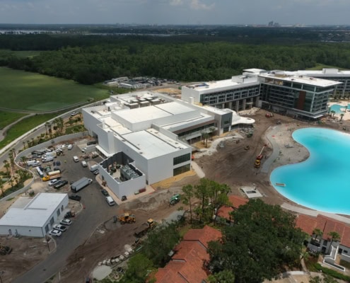 Modern hotel construction site with a large swimming pool, surrounded by greenery and ongoing building activities, showcasing contemporary architecture and real estate development.